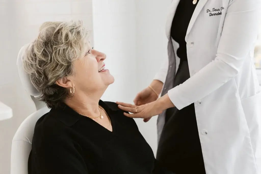 older-woman-smiling-while-seated-in-treatment-chair-as-clinician-in-white-coat-places-hand-on-shoulder-1